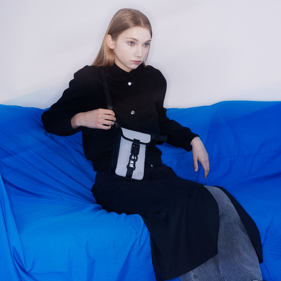 Model sitting on a blue couch, holding a stylish and sustainable crossbody bag, highlighting modern eco-friendly fashion by WAVEIT.