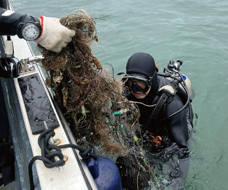 A diver removing abandoned fishing nets and debris from the ocean during a beach ghost net cleanup activity.