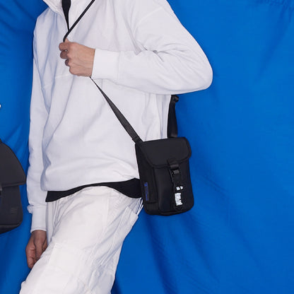 Model wearing a black WAVEIT eco-friendly crossbody bag paired with a white outfit, displayed against a blue background.