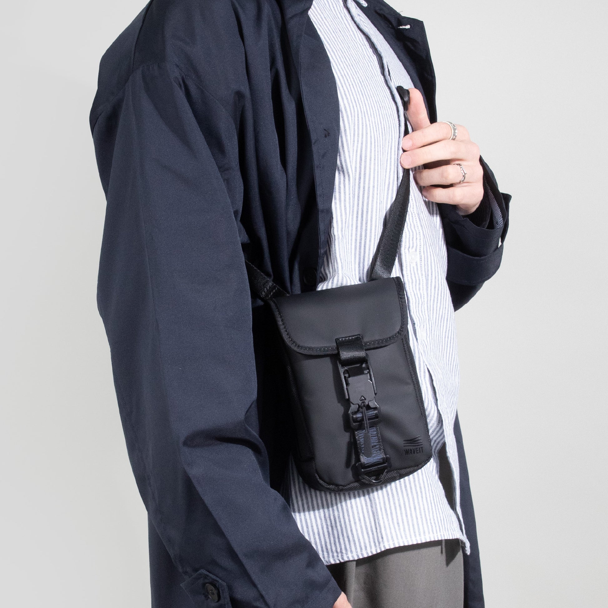 Model wearing a black WAVEIT eco-friendly crossbody bag with secure buckle and adjustable strap.