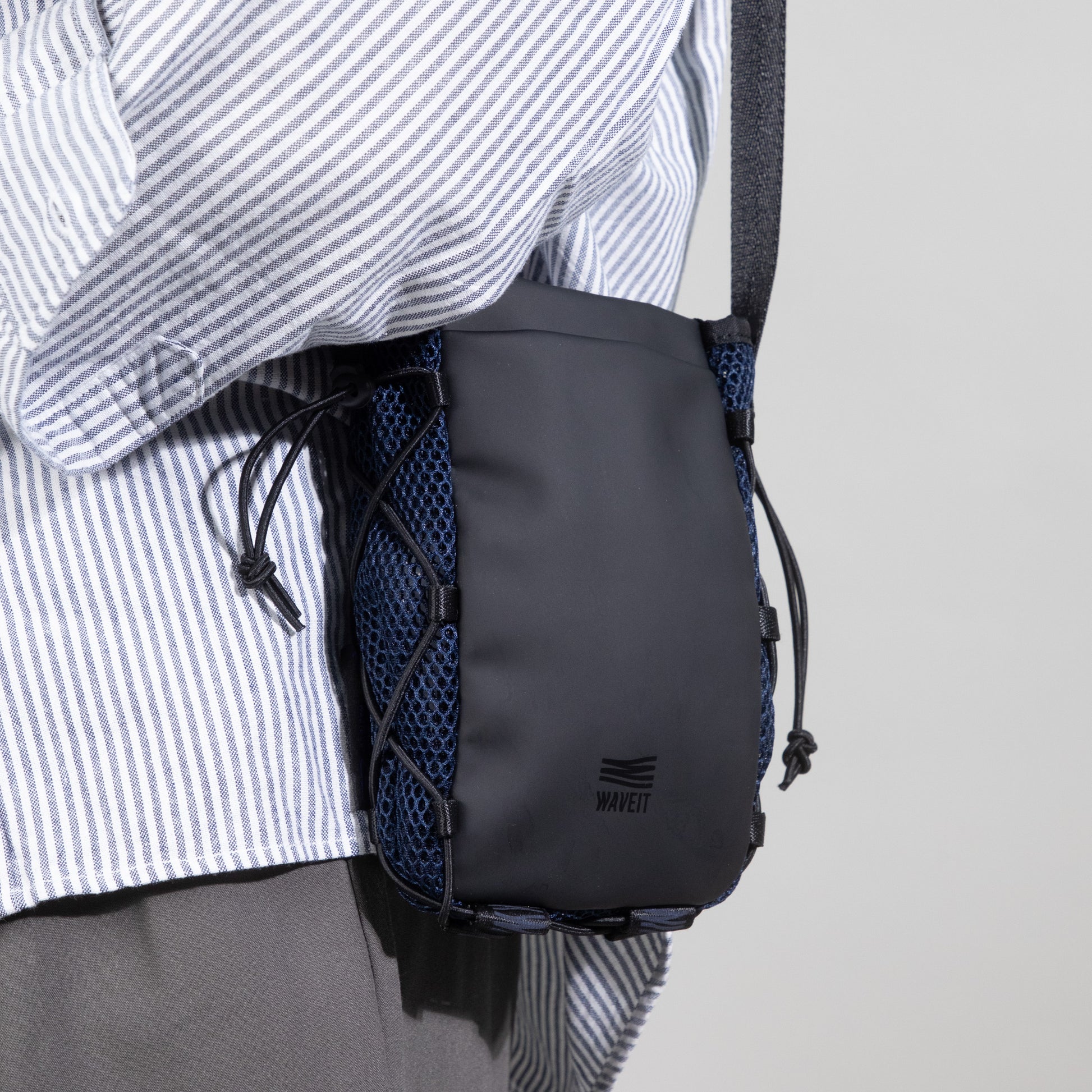 Side view of a WAVEIT crossbody bag in black, worn by a model. The bag features a blue mesh pocket on the side, adding functionality and style.