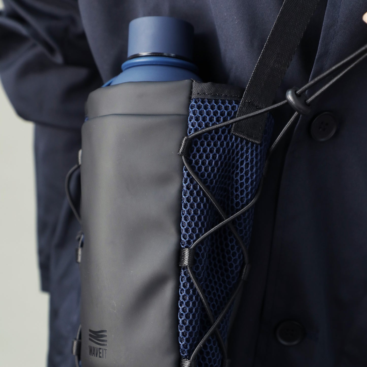 Close-up view of the WAVEIT crossbody bag in black, featuring a blue water bottle securely held in the side mesh pocket.