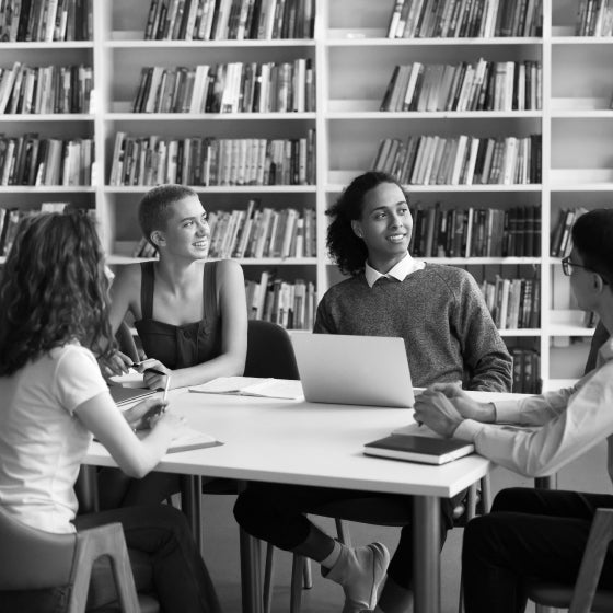 Group of diverse students studying together at a table in a library, discussing and working on a project.